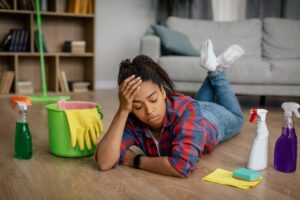 unhappy-young-black-female-rubber-gloves-lies-floor-with-cleaning-supplies-living-room-interior_116547-35427